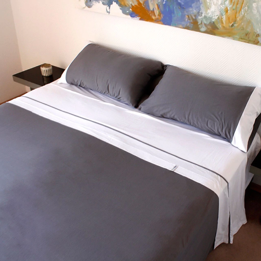 Cama tendida con el juego de sábanas Tromen, gris y blanco