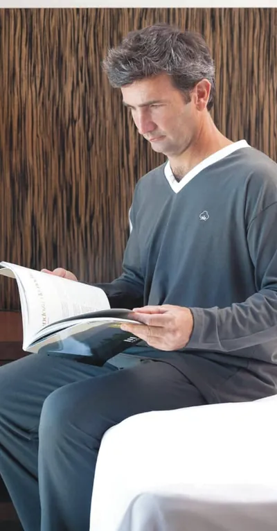 Hombre con pijama de jersey gris, leyendo en la cama